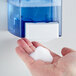 A person's hand with a blue foamy object from a Noble Chemical Free & Clear foaming hand soap dispenser.