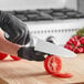 A person in black gloves using a Choice 8" Serrated Chef Knife to cut a tomato.