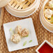 A plate with two steamed Passport Cuisine Pork Shumai and a bowl of sauce.