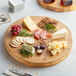 A Front of the House ROOT wooden serving board with cheese, crackers, and other food on it.