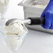 A person in blue gloves using an OXO Good Grips stainless steel ice cream scoop to scoop ice cream into a glass bowl.