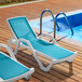 Two Lancaster Table & Seating white chaise lounges with turquoise sling seats next to a pool.
