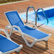 Two Lancaster Table & Seating white chaise lounges with blue sling seats next to a pool.