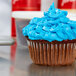 A close-up of a Hoffmaster white fluted baking cup with a cupcake with blue frosting inside.