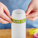 A person holding a Choice silicone squeeze bottle label band on a bottle of olive oil.