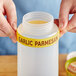 A person using a white silicone label band on a jar with a yellow "Garlic Parmesan" label.
