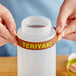 A person's hand holding a silicone label band that says "Teriyaki" around a plastic bottle.