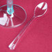 A clear plastic spoon next to a clear plastic spoon on a table with a clear glass stem filled with a clear liquid.