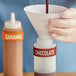 A gloved hand using a Chocolate Silicone Squeeze Bottle to pour chocolate into a container.