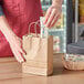 A person putting a packet into a brown natural kraft paper shopping bag with handles.