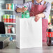 A woman in an apron putting a green soda bottle into a white paper shopping bag.