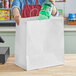 A woman holding a plastic bottle in a white paper shopping bag with handles.