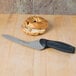 A bagel with a hole in the middle and a Dexter-Russell DuoGlide bread knife on a wooden surface.