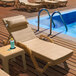 A Lancaster Table & Seating sand resin chaise with a beige cushion and pillow next to a pool.