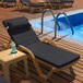 A Lancaster Table & Seating sand resin chaise with a black cushion and pillow on a pool deck.