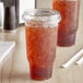 Two Choice clear plastic cups with brown liquid and strawless lids on a table.