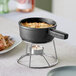 A Valor pre-seasoned cast iron fondue pot of food on a stand over a candle.