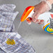 A hand holding a SC Johnson Shout triple-acting laundry stain remover spray bottle and spraying a stain on a shirt.