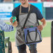A man opening a Choice navy insulated cooler bag full of cans on a baseball field.