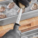 A person using a Choice 4" Galveston Style Oyster Knife with black gloves to open oysters.