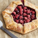 A pie with raspberries and a spoon on a table with a bag of Bob's Red Mill Whole Wheat Pastry Flour.