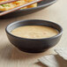 A black matte round melamine ramekin filled with sauce on a table.