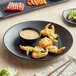 A GET Nara black matte melamine plate with shrimp and dipping sauce on it.
