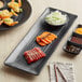 A black GET Nara rectangular melamine platter with sushi, shrimp and other food on a table.
