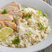 A white plate of rice and chicken with a lime wedge.