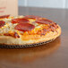 A pepperoni pizza on a white corrugated cardboard circle on a table.