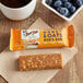 A Bob's Red Mill Peanut Butter Honey & Oats bar on a table with a bowl of oatmeal.