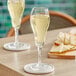 Two Acopa Select tulip flute glasses filled with champagne on a table.