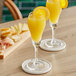 Two Acopa Select tulip flute glasses filled with yellow liquid on a table with cheese and crackers.