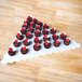 A white triangle display tray with small chocolate cupcakes and raspberries on top.