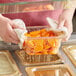 A person using a white towel to cover a Cambro amber plastic food pan filled with carrots.