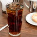 A Libbey paneled cooler glass of iced tea on a table with a bagel.