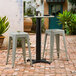 A Lancaster Table & Seating Excalibur black outdoor table base with a black pole on a brick patio with stools
