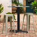 A black Lancaster Table & Seating outdoor table base with a white table on a brick patio.