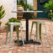A Lancaster Table & Seating Excalibur outdoor table base with stools on a brick patio.