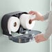 A hand putting a Lavex Select Little Big Roll toilet tissue roll into a dispenser.