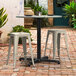 A Lancaster Table & Seating Excalibur outdoor table with stools on a brick patio.