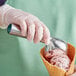 A person in gloves holding a Choice aluminum ice cream scoop filled with ice cream.