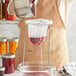 A person pouring red liquid from a Fox Run Jelly and Jam Strainer into a glass jar.