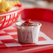 A Genpak paper souffle cup filled with ketchup on a red and white checkered tablecloth.