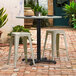 A Lancaster Table and Seating outdoor table base with two stools on a brick patio.