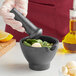 A person using a Fox Run black cast iron mortar and pestle to grind ingredients in a black mortar.