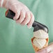 A person in gloves using a black and gold Choice 20 ice cream scoop to scoop ice cream.