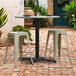 A Lancaster Table & Seating Excalibur outdoor table base with 3 stools on a brick patio.