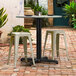 A Lancaster Table & Seating Excalibur outdoor table base with FLAT Tech levelers on a brick patio with stools.