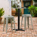 A Lancaster Table & Seating Excalibur outdoor table base with stools on a brick patio.